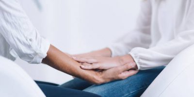 Female Theta healing therapist performing alternative therapy treatment with young woman patient. Therapist holding hands and transfer energy. Wearing white clothes.